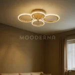 Luminaria Dasha Gold instalada en sala moderna. Su forma circular doble y su tono dorado aportan un toque elegante al espacio, creando un efecto visual sofisticado y acogedor. Ideal para quienes buscan una iluminación decorativa y moderna.