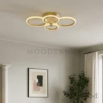 Luminaria Dasha Gold instalada sobre comedor elegante. Su estructura de tres aros metálicos distribuye la luz de forma armónica, destacando la decoración y generando un ambiente acogedor para reuniones o cenas.