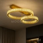 Luminaria Annelie Gold instalada en una sala moderna, iluminando el ambiente con su acabado dorado brillante y diseño de doble aro. Su luz LED de 45W aporta calidez y estilo a espacios contemporáneos.