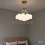 Moon Gold instalada en una sala moderna con tonos neutros, destacando por su iluminación cálida y su diseño elegante de múltiples esferas suspendidas.