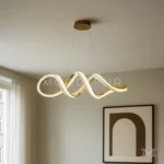 Luminaria Vittora Gold instalada sobre comedor moderno. Su diseño ondulado y dorado brillante se convierte en el centro de atención del ambiente, aportando sofisticación y estilo contemporáneo. Perfecta para iluminar mesas amplias o áreas sociales.