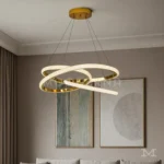 Luminaria Avéne Gold instalada sobre sala con tonos neutros. El acabado satinado y la forma fluida destacan en ambientes minimalistas, aportando un brillo delicado y moderno. Ideal para interiores de alto diseño.