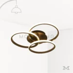 Luminaria Selene Black en fondo blanco con diseño de tres aros entrelazados en acabado negro mate con detalles dorados. Su luz LED integrada aporta un estilo moderno, decorativo y elegante ideal para salas, estudios y dormitorios contemporáneos.