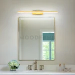 Sigrid Gold instalada sobre un espejo de baño minimalista, destacando su acabado dorado y su iluminación cálida funcional.