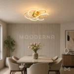 Luminaria LED Lota Gold dorada instalada sobre comedor moderno con mesa y sillas