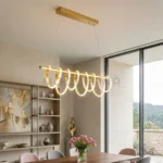 Lámpara colgante LED dorada para comedor Ariel Gold sobre mesa de madera