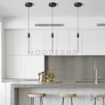 Tres lámparas colgantes Misaki Black instaladas sobre isla de cocina moderna con barra de concreto.