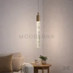 Lámpara colgante dorada Misaki Gold con luz cálida junto a un sofá en una sala moderna.