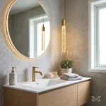 Lámpara colgante Misaki Gold dorada junto a un espejo redondo y lavamanos de baño moderno.