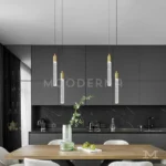 Cuatro lámparas colgantes Misaki Gold doradas instaladas sobre una mesa de cocina moderna.