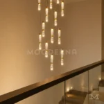 Detalle de lámpara Sienna Gold con luces cilíndricas doradas y efecto de iluminación cálida en escalera.